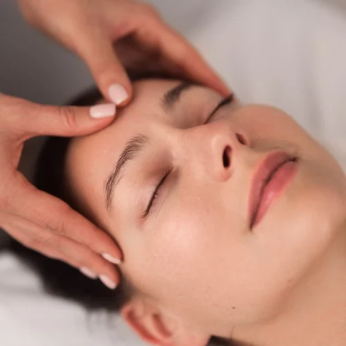 From above of crop unrecognizable cosmetician massaging forehead of young female client lying on couch with closed eyes during facial procedure in light salon From above of crop unrecognizable cosmetician massaging forehead of young female client lying on couch with closed eyes during facial procedure in light salon